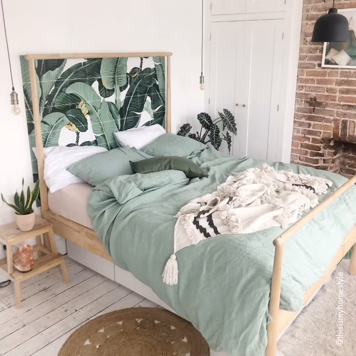 IXXI of banana leaves set into the wooden headboard of a bed, with green bedding in front of it