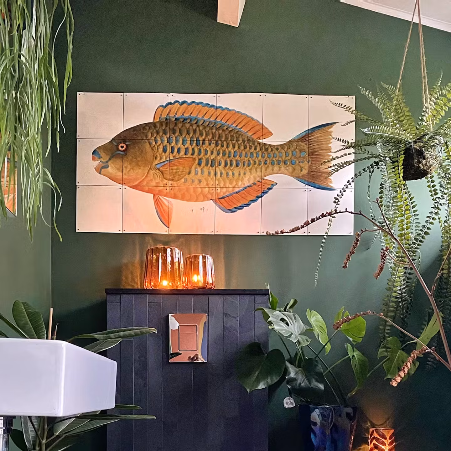 IXXI of a parrotfish on a dark green bathroom wall, above a black cabinet between hanging plants