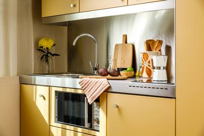 Modern kitchen with yellow cabinets, stainless steel countertop, cutting board, avocados, lime, wooden utensils, and a flower in a vase.