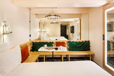 Hotel room with a bed, a corner seating area with colourful cushions, and a small table set for coffee. A large mirror reflects the space.