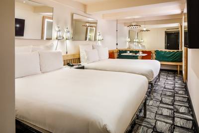 Modern hotel room with two double beds, abstract carpet, wall lamps, and large mirrors, creating a cozy and stylish atmosphere.