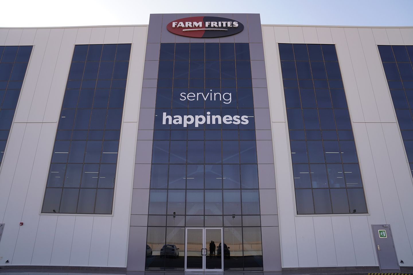 Facade of Farm Frites building with large windows and the slogan "serving happiness" displayed prominently.