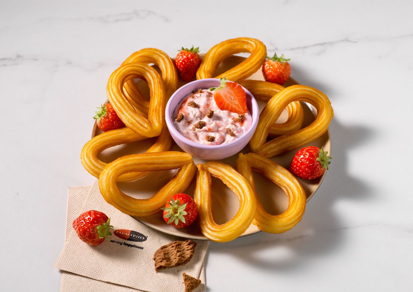 Golden churros arranged in a circle with fresh strawberries and a bowl of strawberry cheesecake topped with strawberry slices in the center.