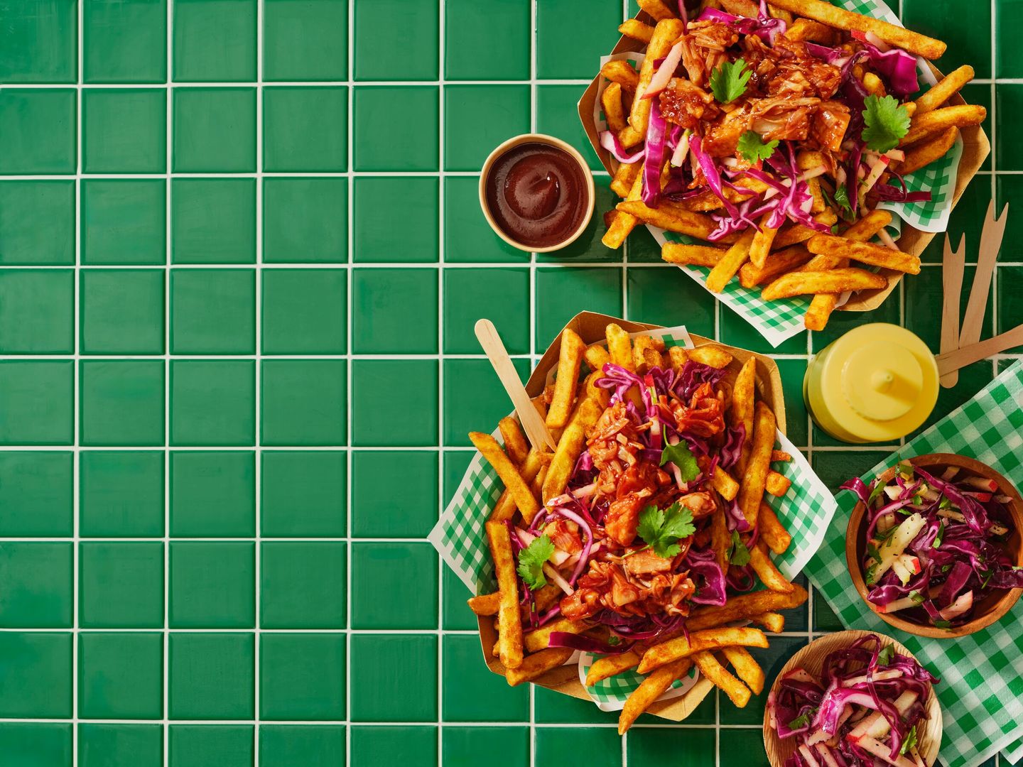 Plates of fries topped with shredded meat and purple cabbage on a green tiled table, with condiments and napkins nearby.