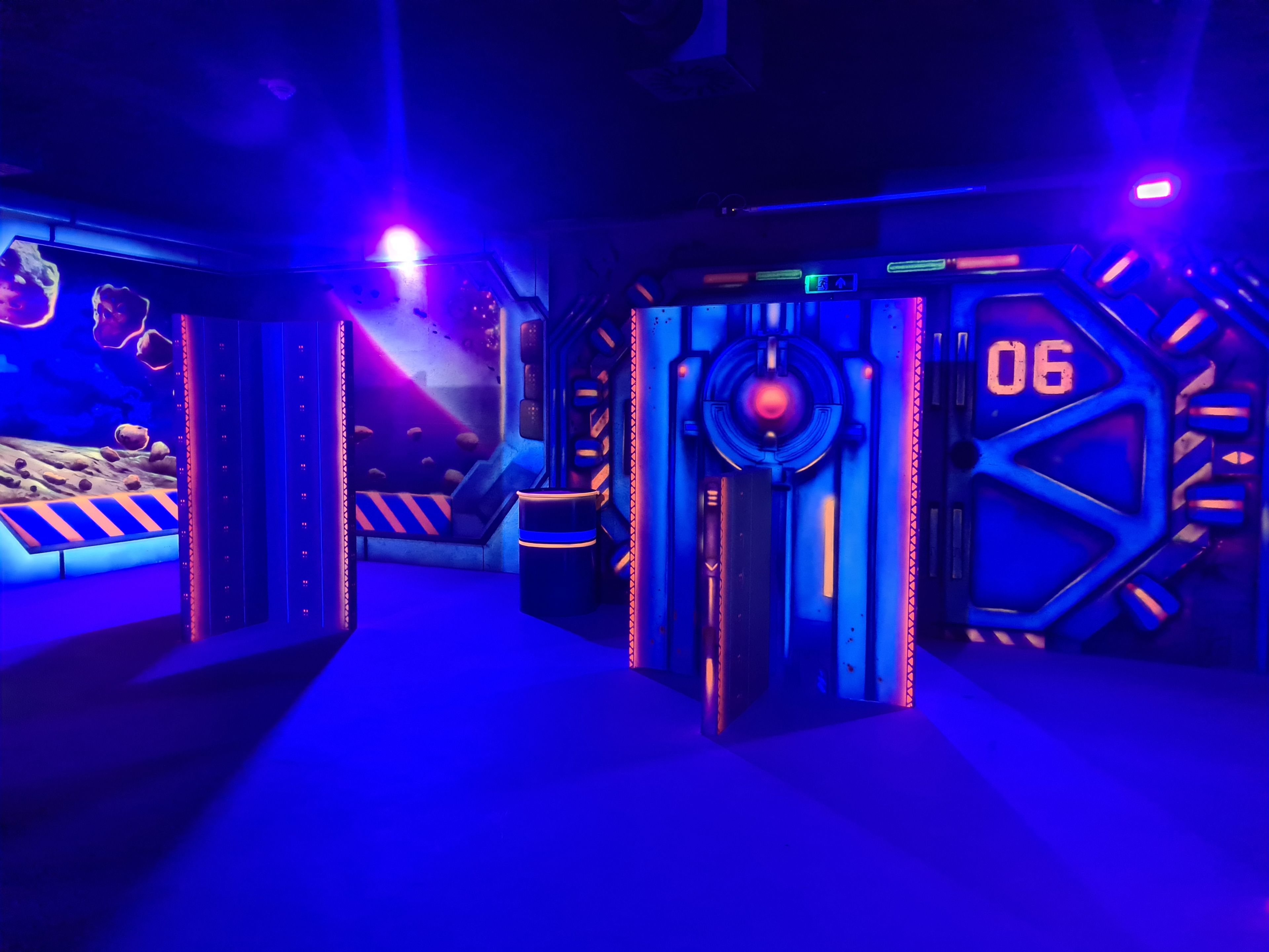 Eine neonbeleuchtete, futuristische Lasertag-Arena mit leuchtenden Wänden, Sci-Fi-Dekor und lebendiger blau-violetter Beleuchtung.