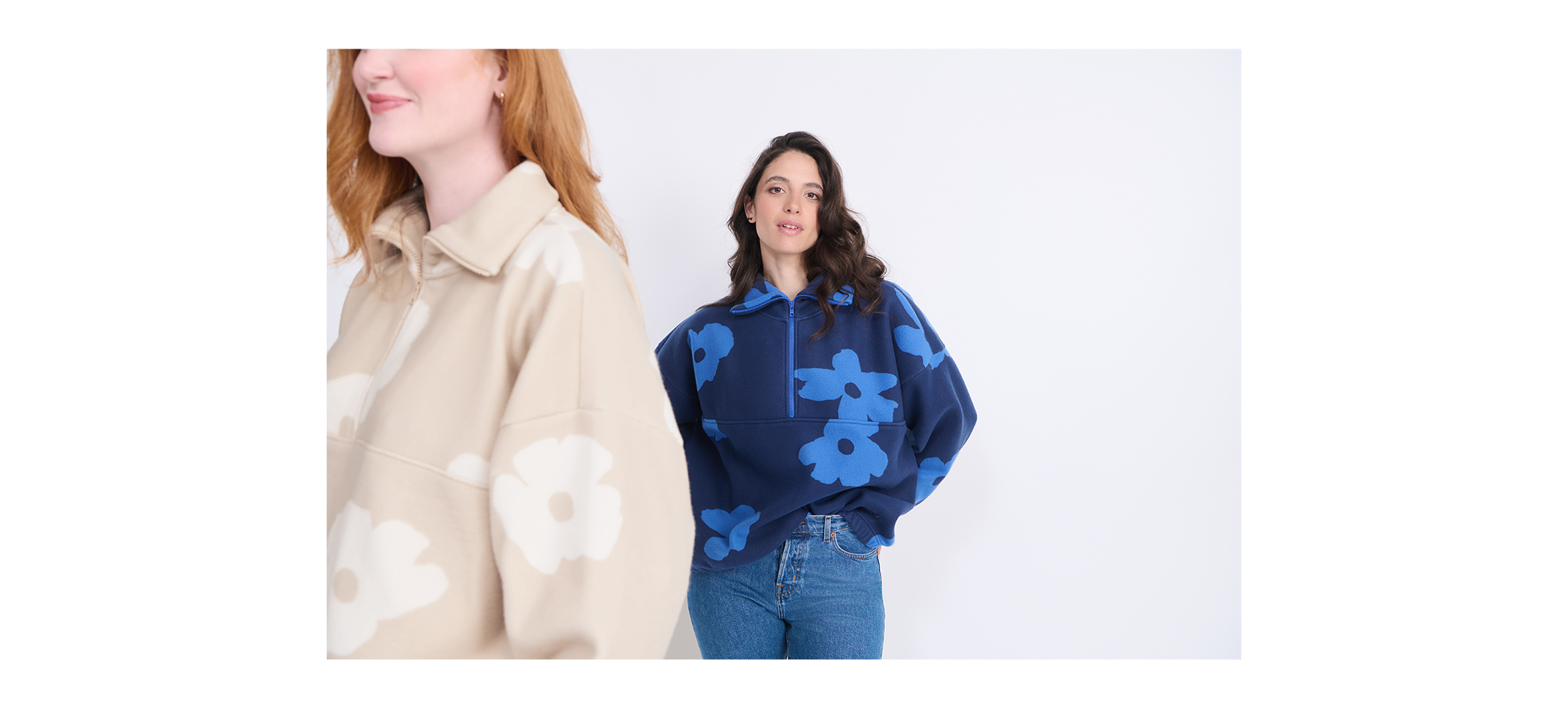 Two women wearing floral patterned tops, one in beige and white, the other in blue and darker blue, standing against a light background.