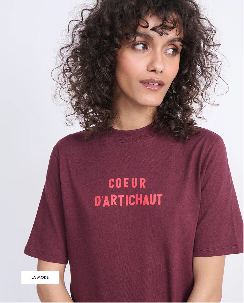 A person with curly hair wearing a maroon shirt with "COEUR D