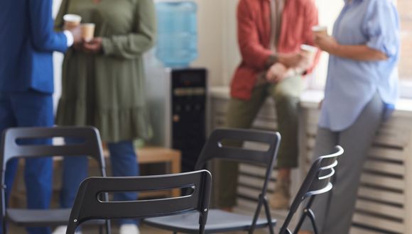 Vier Personen, die während einer Pause locker herumstehen. Im Vordergrund sind Stühle zu sehen.