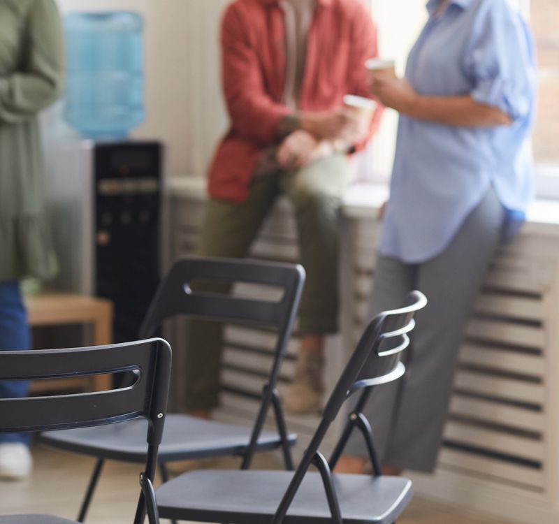 Vier Personen, die während einer Pause locker herumstehen. Im Vordergrund sind Stühle zu sehen.