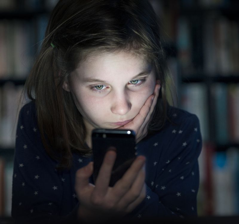 Mädchen, das mit einem kritischen Blick auf sein Handy schaut.