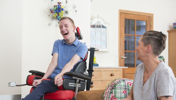 Junger Mann im Rollstuhl und eine Frau lachen gemeinsam