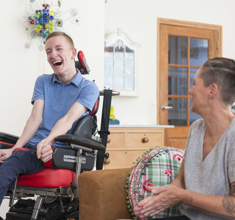 Junger Mann im Rollstuhl und eine Frau lachen gemeinsam