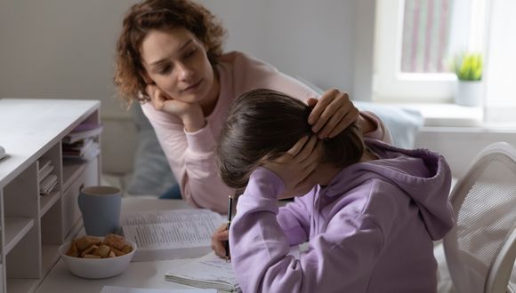 Mutter sitzt am Tisch bei ihrer Tochter, die Hausaufgaben macht.