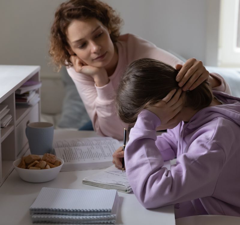 Mutter sitzt am Tisch bei ihrer Tochter, die Hausaufgaben macht.