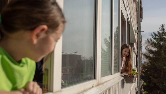Zwei Kinder schauen aus dem Fenster und blicken sich an.