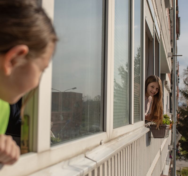 Zwei Kinder schauen aus dem Fenster und blicken sich an.