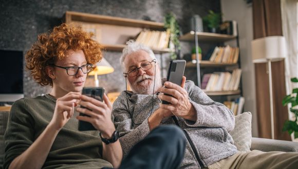 Älterer Mann zeigt jüngerem Mann etwas auf seinem Smartphone.