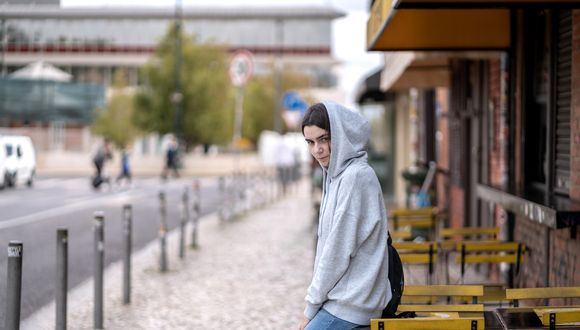 Junge Frau lehnt sich an den Tisch eines Strassencafés und schaut abwartend in die Kamera.