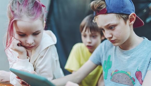 Drei Kinder schauen sich etwas auf einem Tablet an.