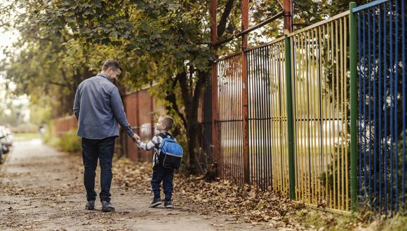 Ein Mann und ein Kind gehen auf dem Trottoir, sie halten sich an den Händen.