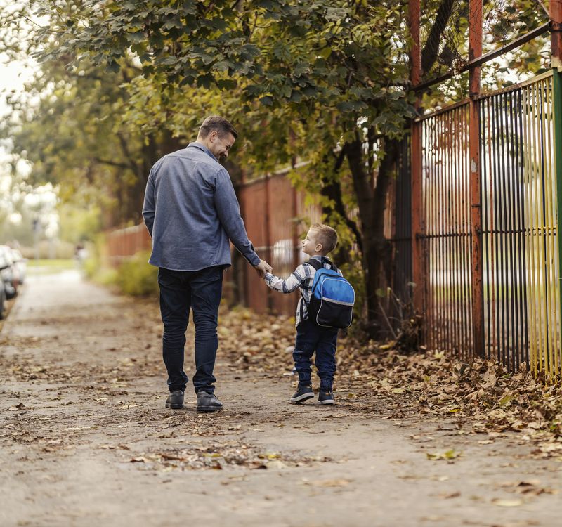 Ein Mann und ein Kind gehen auf dem Trottoir, sie halten sich an den Händen.