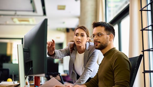 Zwei Mitarbeitende diskutieren vor dem Computer über Unternehmensarchitektur.