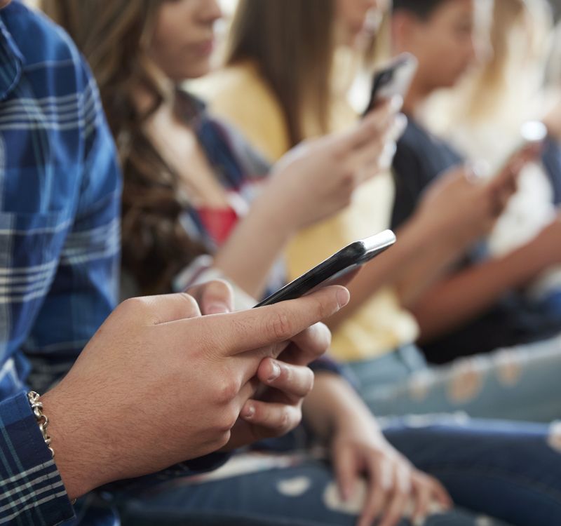 Jugendliche sitzen in einer Reihe und sind in ihre Smartphones vertieft.