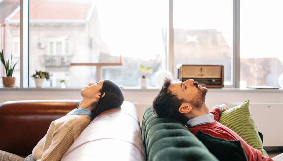 Zwei Menschen sitzen einander rücklings zugewandt auf je einem Sofa.