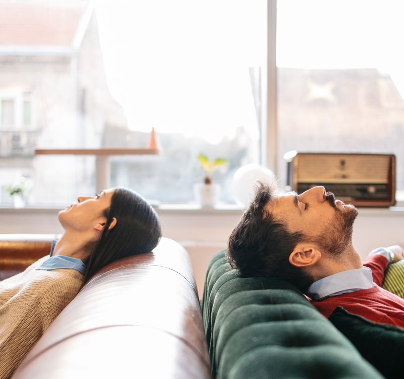Zwei Menschen sitzen einander rücklings zugewandt auf je einem Sofa.
