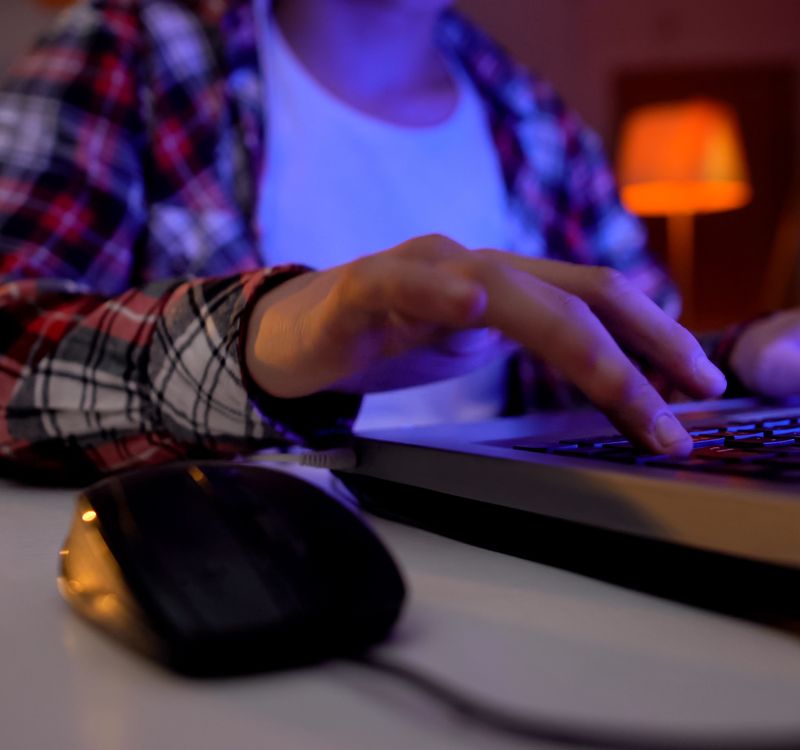 Jüngere männliche Person sitzt am Tisch und gibt etwas in die Tastatur des Laptops ein.
