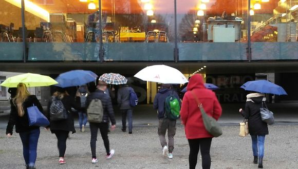 Eine Gruppe von Menschen geht auf ein Gebäude zu. Es regnet.