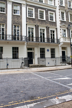 georgian terraced house with yellow London brick and cream rendered windows with black railings. A blue plaque to the left of the front door and window