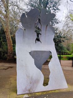 a large metal abstract sculpture next to park gates with trees in the background.