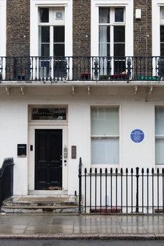frontage of georgian terraced house in London. Yellow brick with black front door. Blue plaque to the right of window