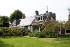 the exterior of a house with a slopping roof and dormer windows surrounded by trees, shrubs and grass