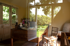 interior of a cabin with the outdoors reflected in the glass window. a writing table and chair are in the middle of the cabin.