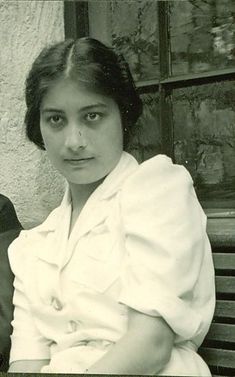 Noor Inayat Khan, a young woman of Indian heritage. Her brown hair is parted and swept back into a bun and she is wearing a white collared dress.