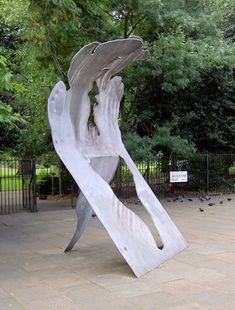 a large metal abstract sculpture next to park gates with trees in the background.