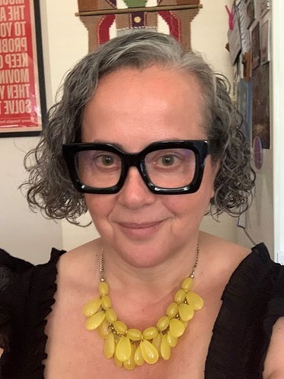 photo portrait of a woman with short curly dark grey hair, black framed glasses, black top and yellow bead necklace
