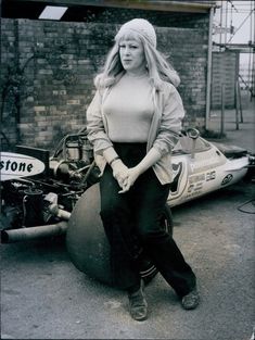 a blond woman is sitting on the wheel of a motor racing car