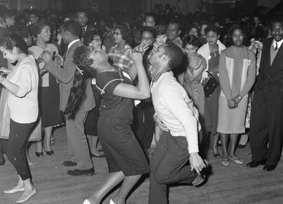 A lively 1950s dance scene with a couple energetically dancing in the foreground, surrounded by a crowd watching and enjoying the music.