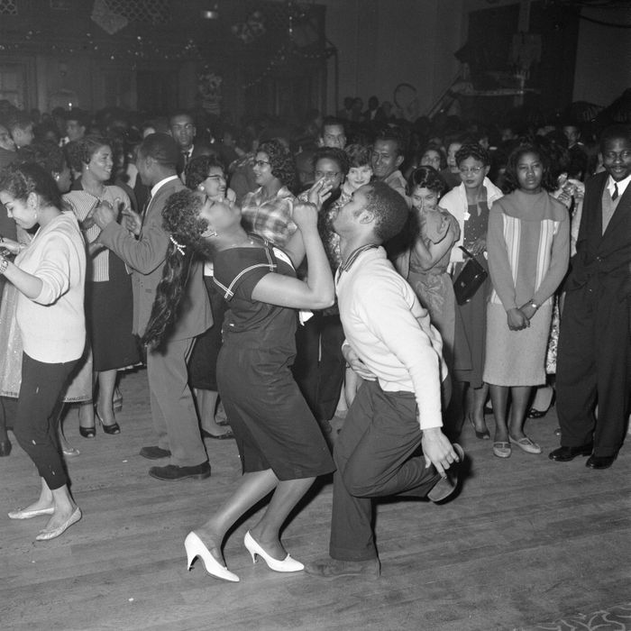 A lively 1950s dance scene with a couple energetically dancing in the foreground, surrounded by a crowd watching and enjoying the music.