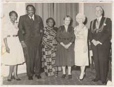 A group of six people, including men and women, standing in formal attire in a decorated room.