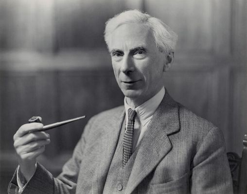 an older white man white white hair and a grey suit holds a long pipe