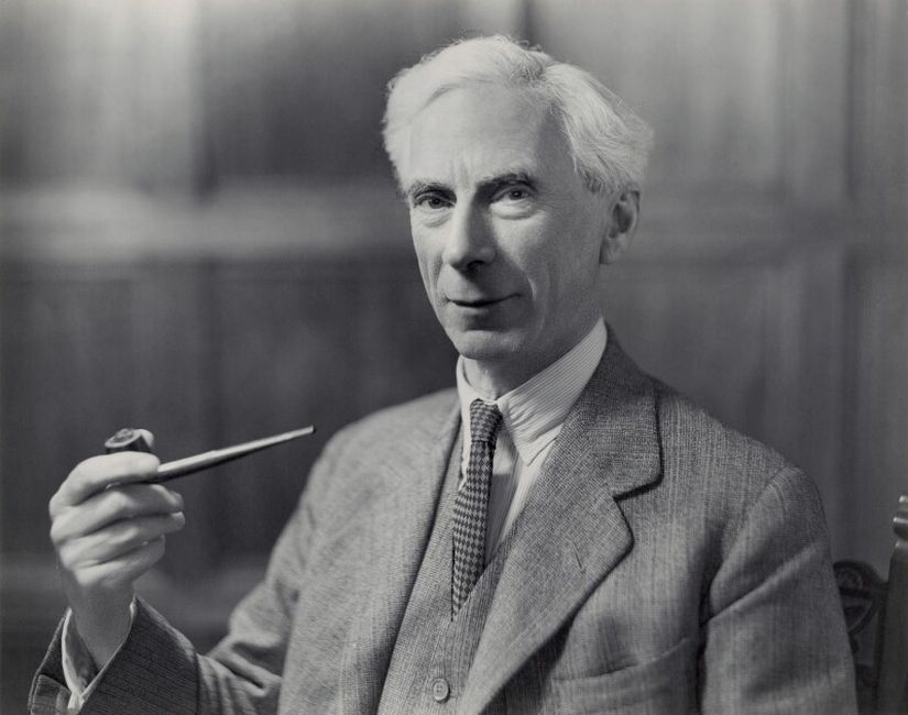 an older white man white white hair and a grey suit holds a long pipe
