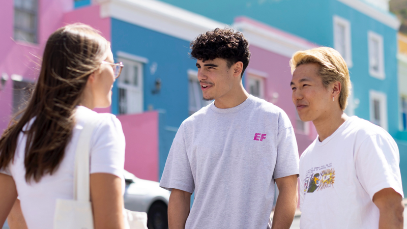 Three EF Language Abroad students talking together in Cape Town’s Bo-Kaap neighborhood, standing in front of its colorful houses on a sunny day.