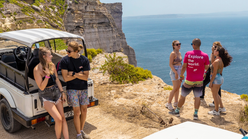 EF Language Abroad students exploring the coast of Malta, standing by open-top jeeps on a cliffside overlooking the Mediterranean Sea during a sunny day trip.