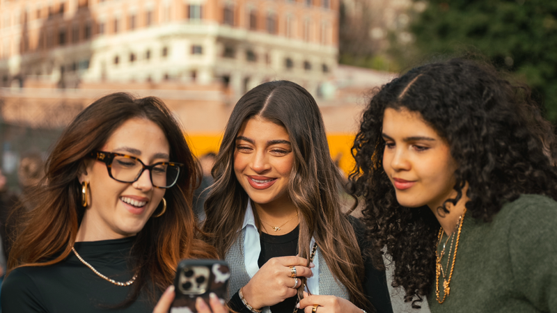 Three EF Language Abroad students in Rome smiling and looking at a phone together while exploring the city on a sunny day.