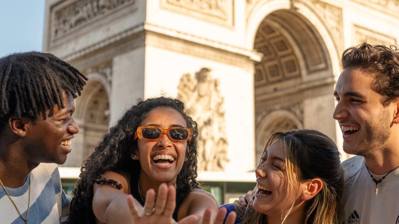 Four EF Language Abroad students laughing together in front of the Arc de Triomphe in Paris while exploring the city on a sunny day.