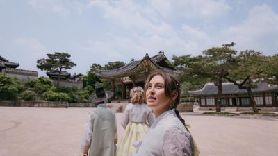 EF Language Abroad students exploring a traditional palace in Seoul, wearing hanbok and walking through historic courtyards surrounded by ornate wooden buildings and pine trees.